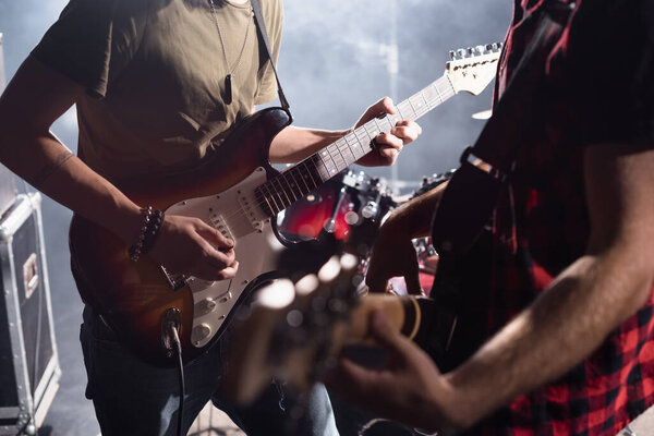 KYIV, UKRAINE - AUGUST 25, 2020: Cropped view of musician playing electric guitar with pick with blurred guitarist on foreground