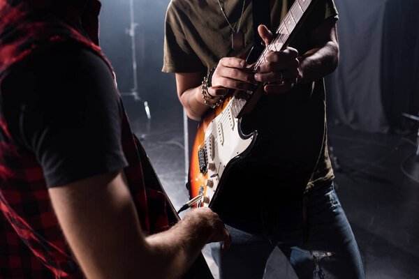 KYIV, UKRAINE - AUGUST 25, 2020: Cropped view of man playing guitar during rock band rehearsal with blurred musician on foreground