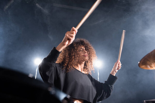 Rock band musician with drumsticks playing on cymbal on blurred foreground