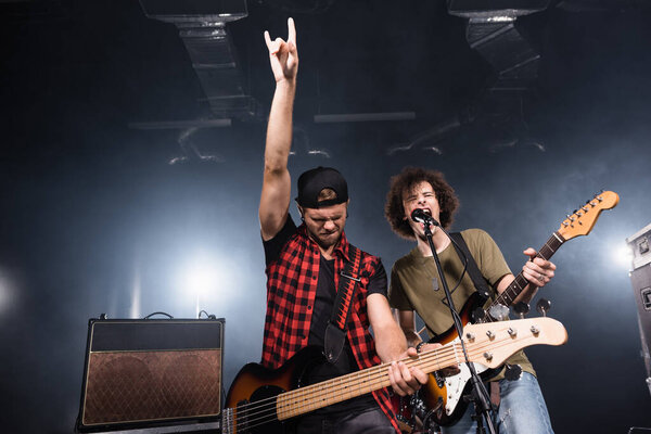 KYIV, UKRAINE - AUGUST 25, 2020: Guitarist with rock gesture standing near musician shouting in microphone with backlit on background