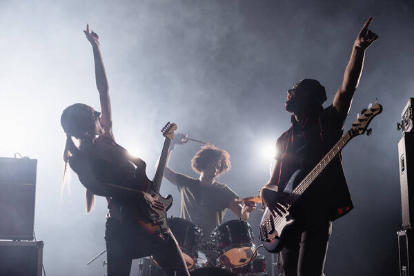 KYIV, UKRAINE - AUGUST 25, 2020: Rock band guitarists with hands in air singing with smoke and drummer on background