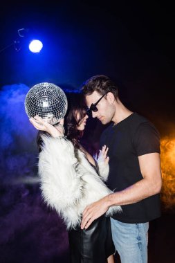 Havada disko topuyla esmer bir kadın erkek arkadaşına dumanla dokunuyor ve siyah ışıkta geçiyor.