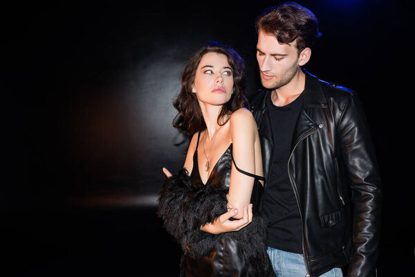 Сексуальная женщина в платье с плечевым ремнем соскальзывает, глядя на страстного бойфренда на черном