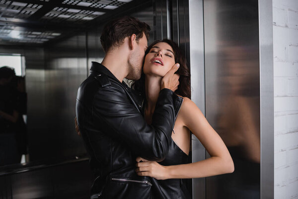 Мужчина в кожаной куртке касается шеи чувственной женщины с закрытыми глазами в лифте