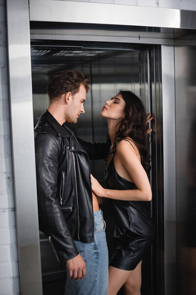 Страстная кудрявая женщина с закрытыми глазами раздевает мужчину в кожаной куртке в лифте