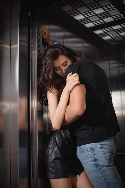 身穿黑色T恤和牛仔裤的充满热情的男人在电梯入口处拥抱着双目紧闭的性感女人 — 图库照片
