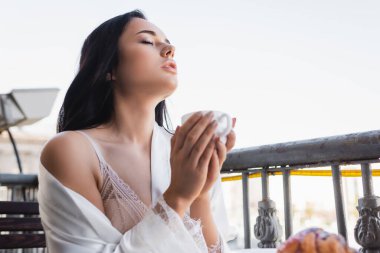 Güzel esmer kadın kapalı gözlerle kahve içmekten zevk alıyor.