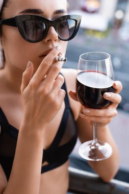 Siyah iç çamaşırlı seksi bir kadın sigara içiyor ve balkonda şarap içiyor.