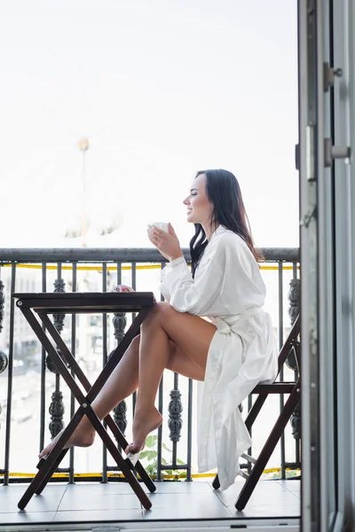 Sonriente Morena Mujer Túnica Blanca Bebiendo Sentado Balcón — Foto de Stock