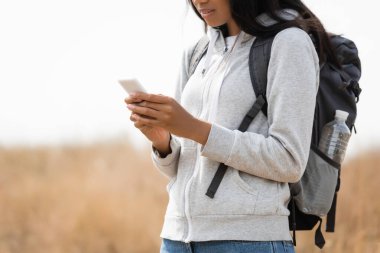 Sırt çantalı Afro-Amerikan yürüyüşçünün açık havada akıllı telefon kullanması.  