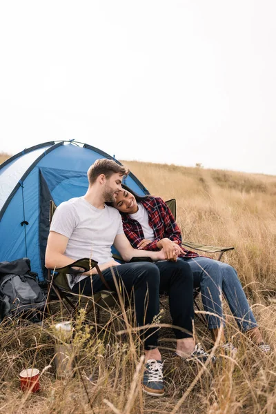 Smiling Multiethnic Couple Holding Hands While Sitting Tent Lawn — Stock Photo, Image