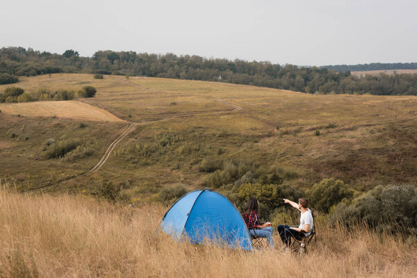 Мужчина указывает пальцем на травянистые холмы рядом с африканской американской подружкой с чашкой и палаткой 