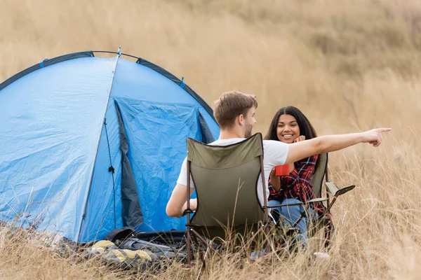 在野外露营时 一个带着杯子走近笑着的非洲裔美国女人的男人 — 图库照片