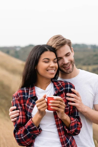 Smiling Man Closed Eyes Hugging African American Girlfriend Cup Outdoors — Stock Photo, Image