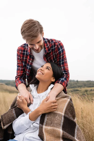 Smiling Man Embracing African American Girlfriend Wrapped Blanket Meadow — Stock Photo, Image