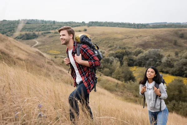 Glimlachende Man Met Rugzak Wandelen Heuvel Buurt Van Afrikaanse Amerikaanse — Stockfoto