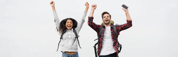 Glada Multietniska Par Med Ryggsäckar Och Smartphone Isolerade Grå Banner — Stockfoto