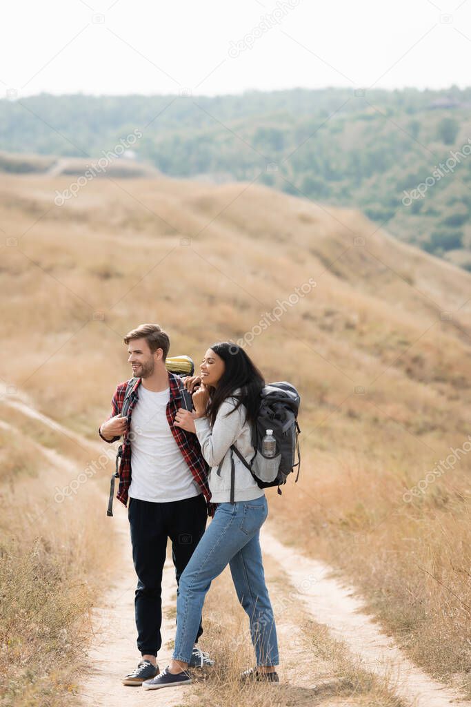 Smiling african american woman with backpack embracing boyfriend while hiking outdoors 