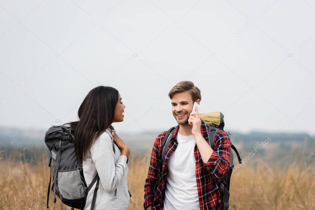 African american woman with backpack standing near boyfriend talking on smartphone outdoors during trip 