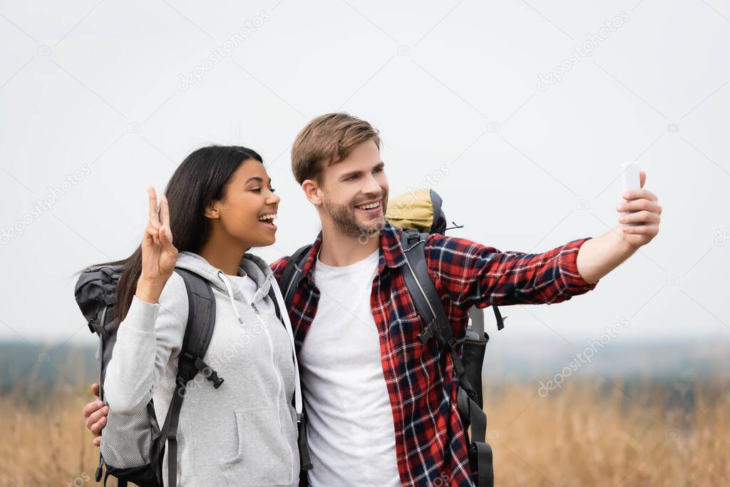 Smiling multiethnic tourists taking selfie with smartphone outdoors 