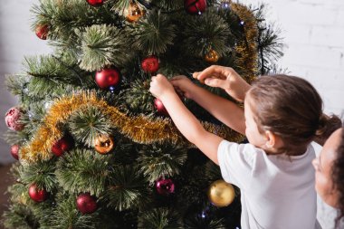 Anne ve kızı evde çam ağacını Noel balosuyla süslüyorlar.