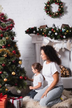Evde çam ve şöminenin yanında oturan anne ve kızın yan görüntüsü