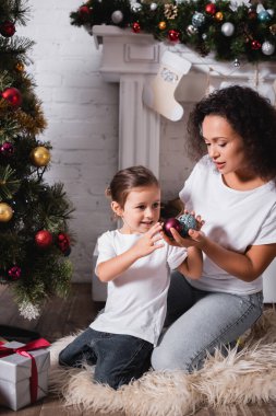 Annesiyle kızı şöminenin yanında noel baloları tutarken ve evde çam yetiştirirken.