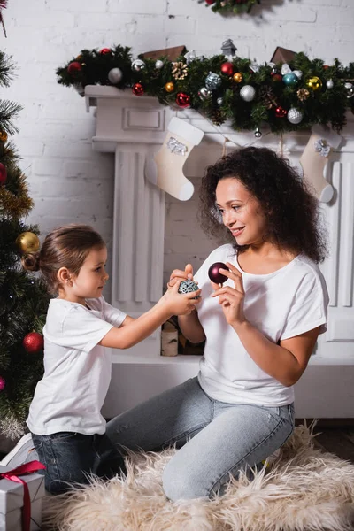 Tochter Und Mutter Mit Weihnachtskugeln Neben Geschmückter Kiefer Und Kamin — Stockfoto