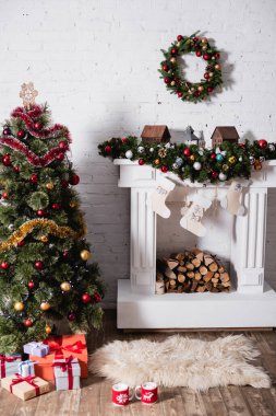 Çam ağacının yanındaki hediye kutuları ve süslü şöminenin üstündeki Noel çelengi.