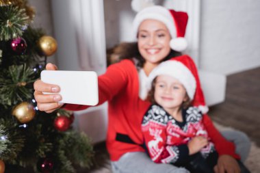 Noel Baba şapkalı anne ve kızının evde selfie çektiği seçici bir odak noktası.