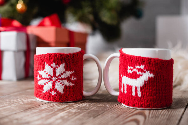 Selective focus of cups with knitted christmas holders on wooden table