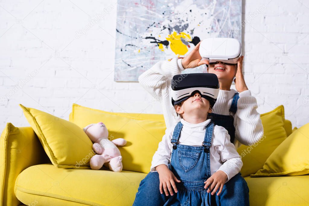  Daughter standing near mother in virtual reality headset at home