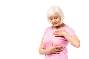 Beyaz tenli, pembe tişörtlü, göğsüne dokunan beyaz saçlı kadın.