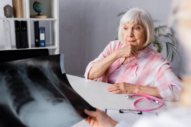 Göğüs röntgeniyle doktorun yanında oturan düşünceli yaşlı kadının seçici odağı.