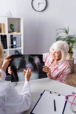 Doktor ve yaşlı kadın iş yerindeki göğüs röntgenine bakıyor.
