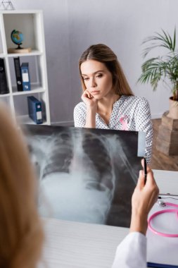 Göğüs röntgeniyle doktorun yanında oturan üzgün yetişkin kadının seçici odağı.