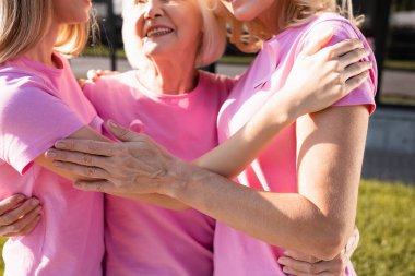 Cropped view of three women in pink t-shirts embracing, concept of breast cancer clipart