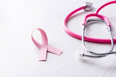 Göğüs kanserinin pembe kurdelesi, beyaz ahşap arka planda steteskop yakınlarında farkındalık.