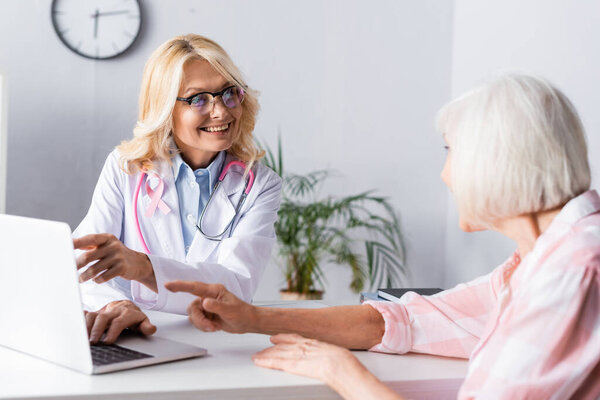 Doctor and patient pointing with fingers and looking at each other near laptop 