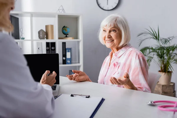 리본을 의사와 노트북 근처에서 대화를 나누는 나이든 여성의 선택적 — 스톡 사진