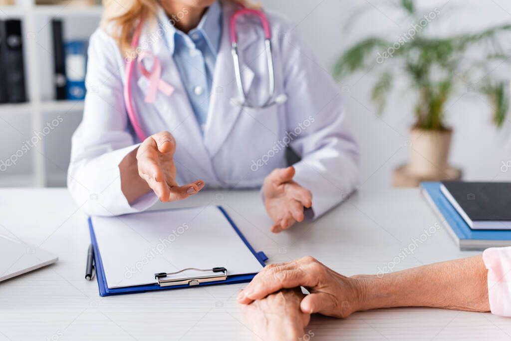 Cropped view of doctor talking to patient while sitting at table in clinic