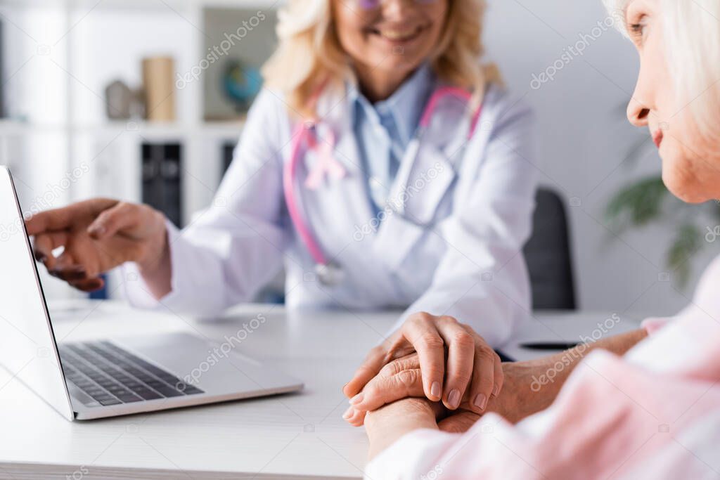 Selective focus elderly woman sitting at table with clenched hands near doctor