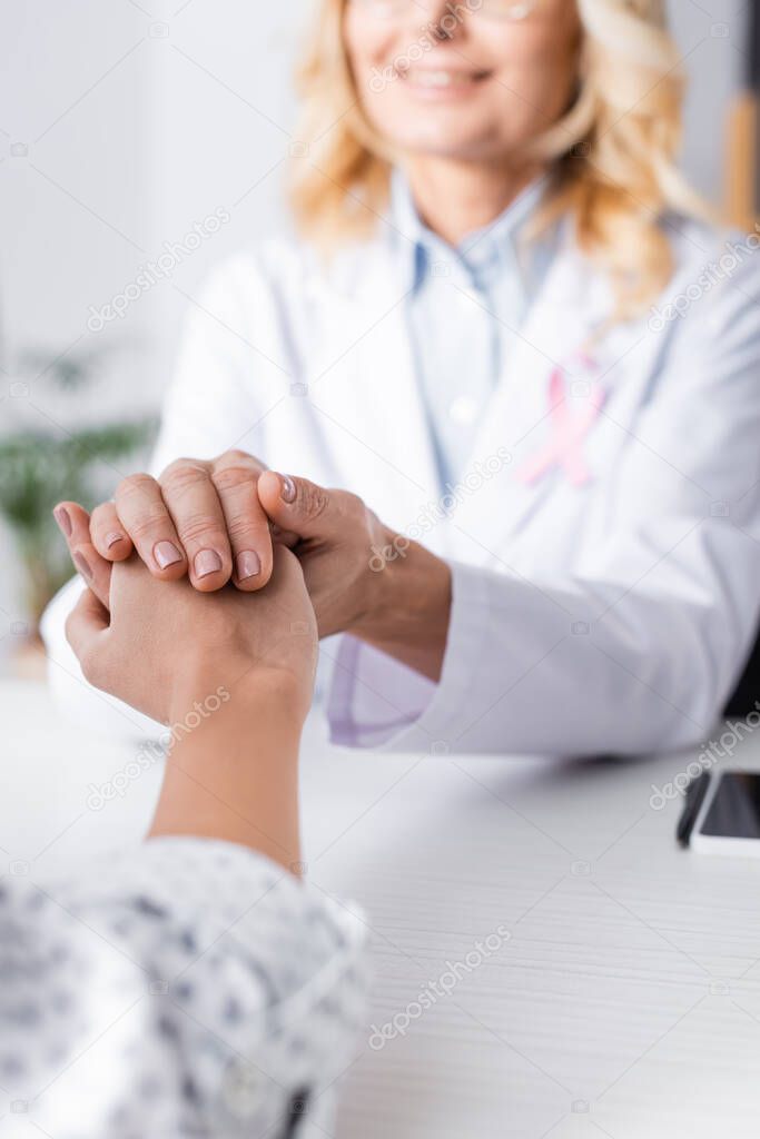 Selective focus of patient holding hand with doctor in white coat 