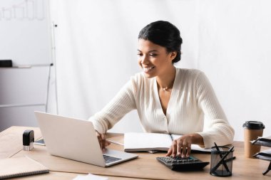 Mutlu Afro-Amerikan kadın bilgisayarına bakarken ofiste hesap makinesinde bulanık arka planda.