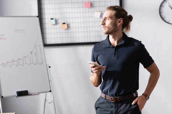 Confident businessman with hand in pocket looking away while standing near flipchart in office