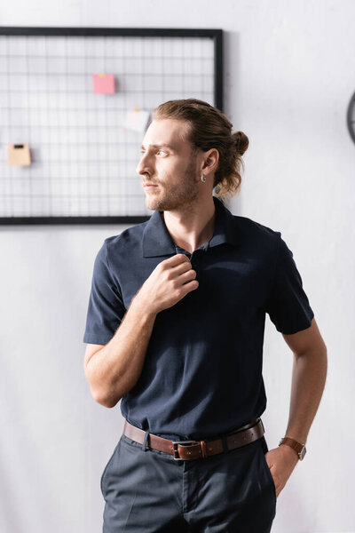 Confident businessman with hand in pocket looking away while standing in office with blurred mesh organizer on background