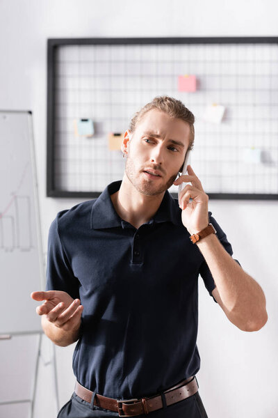 Confident businessman gesturing while talking on phone in office on blurred background