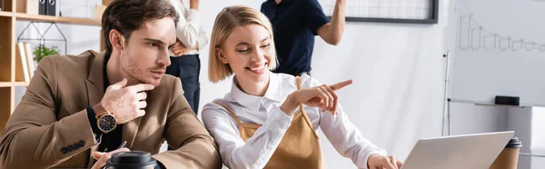 Орієнтований Чоловік Дивиться Ноутбук Сидячи Поруч Щасливою Жінкою Вказуючи Пальцем — стокове фото