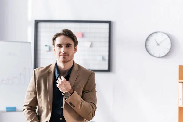 Hombre Negocios Sonriente Mirando Cámara Mientras Toca Cuello Camisa Oficina — Foto de Stock