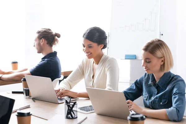 Smiling Multicultural Female Workers Typing Laptops While Sitting Desk Colleague — Stock Photo, Image